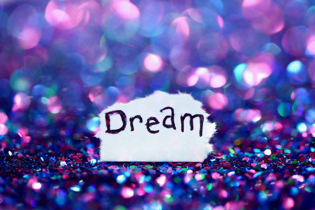 A simple message to dream with shimmery purple and pink glitter bokeh. by Dream and Meaning Dream signage surrounded sequins