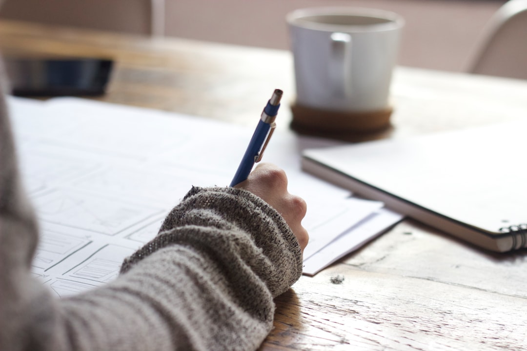Designer sketching Wireframes by Dream and Meaning person writing on brown wooden table near white ceramic mug