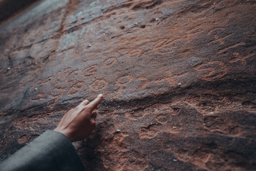 Thamudic Inscription, Nature Reserve – NEOM, Saudi Arabia | In NEOM, thousands of inscriptions have been found etched onto stone, giving us a unique window into the linguistic diversity and richness of ancient Arabia. by Dream and Meaning a person pointing at a rock with writing on it